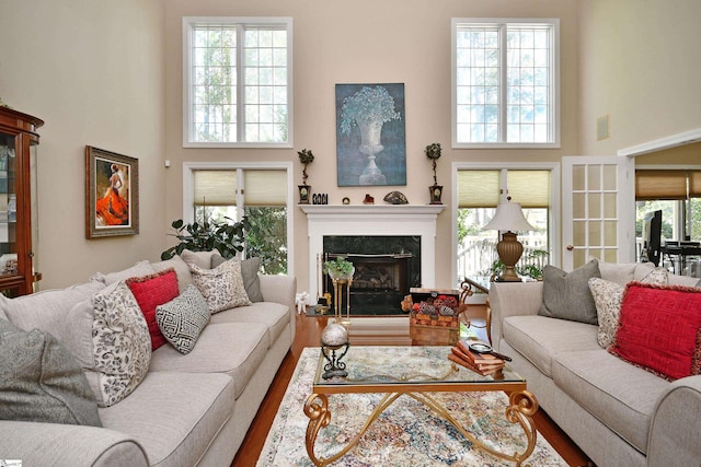 living room with a high end fireplace, hardwood / wood-style floors, a towering ceiling, and plenty of natural light