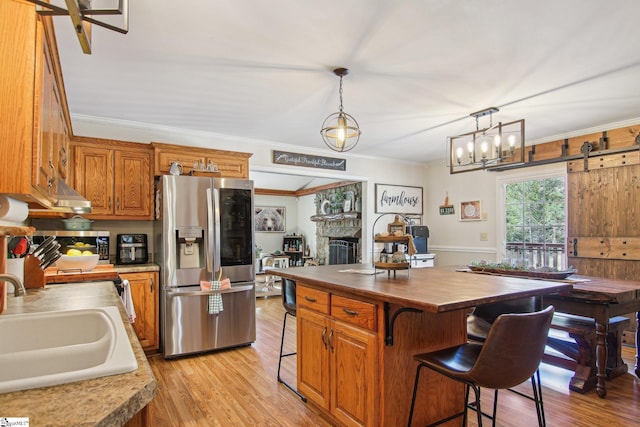 kitchen with stainless steel fridge with ice dispenser, butcher block counters, a kitchen island, sink, and pendant lighting