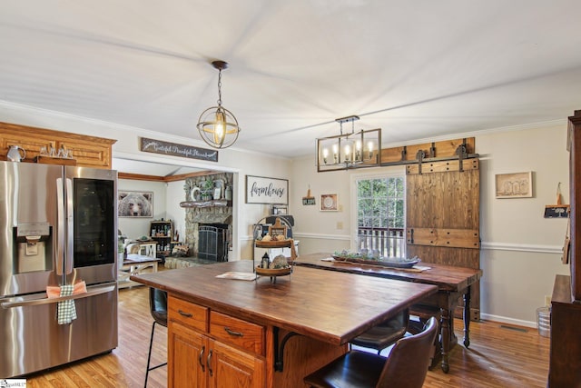 kitchen with light hardwood / wood-style flooring, a breakfast bar area, pendant lighting, stainless steel fridge, and a barn door