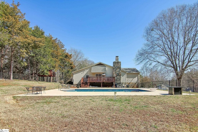 rear view of house with an outdoor fire pit, a lawn, and a pool side deck