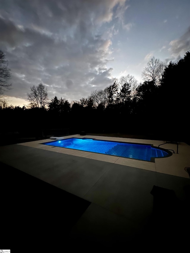 pool at dusk with a patio and a diving board