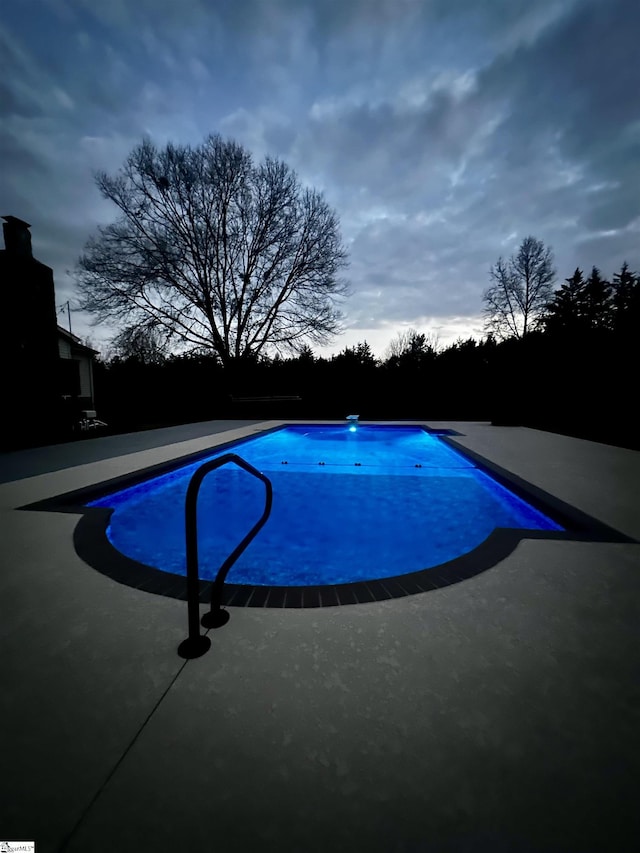 pool at dusk with a patio area and a diving board