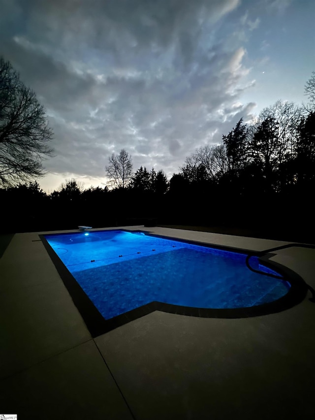 pool at dusk featuring a patio and a diving board