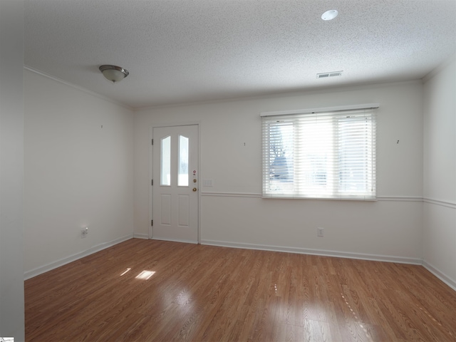 foyer entrance with wood-type flooring, a textured ceiling, and ornamental molding