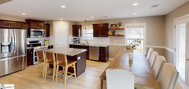 kitchen with appliances with stainless steel finishes, sink, a center island, light hardwood / wood-style floors, and hanging light fixtures