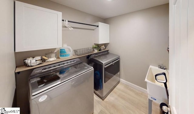 laundry area with light hardwood / wood-style flooring, washer and dryer, and cabinets