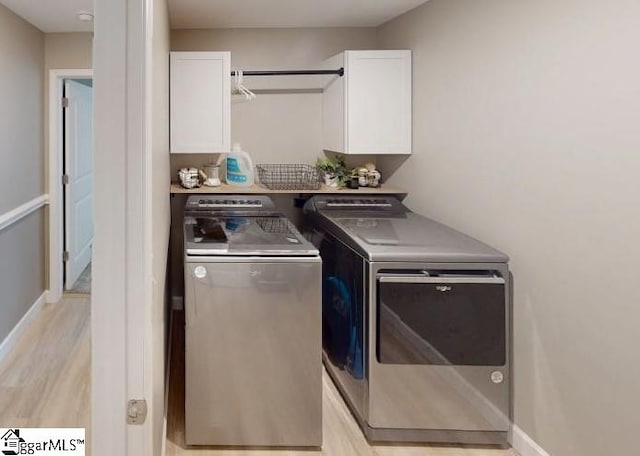 washroom featuring cabinets, washer and clothes dryer, and light hardwood / wood-style flooring