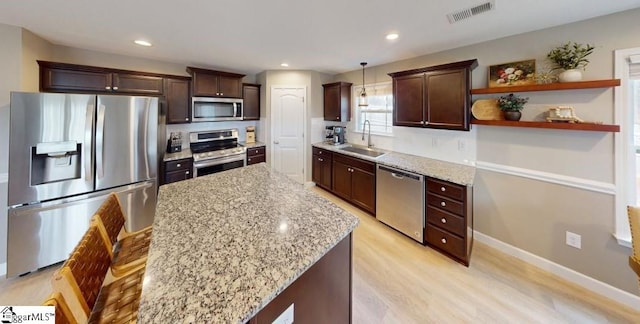 kitchen featuring stainless steel appliances, light stone counters, light hardwood / wood-style floors, pendant lighting, and sink