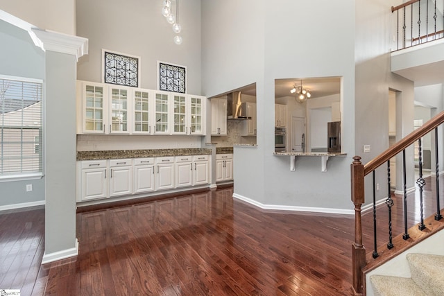 kitchen with white cabinetry, dark wood-type flooring, appliances with stainless steel finishes, wall chimney exhaust hood, and pendant lighting