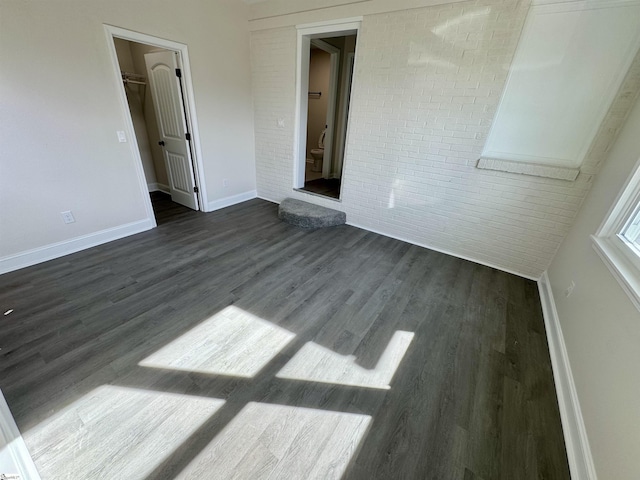 interior space with brick wall, dark hardwood / wood-style floors, and a walk in closet