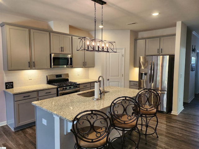 kitchen with appliances with stainless steel finishes, a center island with sink, light stone counters, decorative light fixtures, and sink