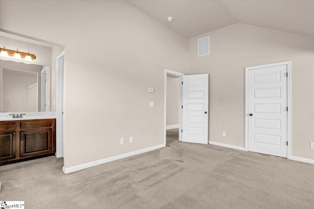 unfurnished bedroom featuring high vaulted ceiling, ensuite bath, light colored carpet, and sink