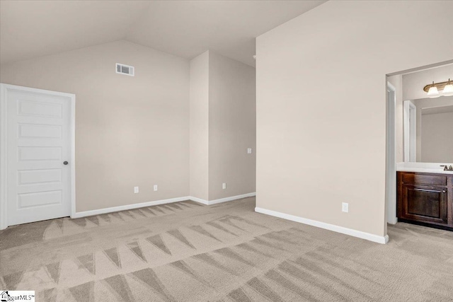 unfurnished bedroom with light carpet, ensuite bathroom, and vaulted ceiling