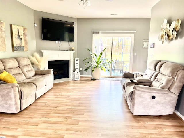 living room with light wood-style flooring, a ceiling fan, a fireplace with flush hearth, and baseboards