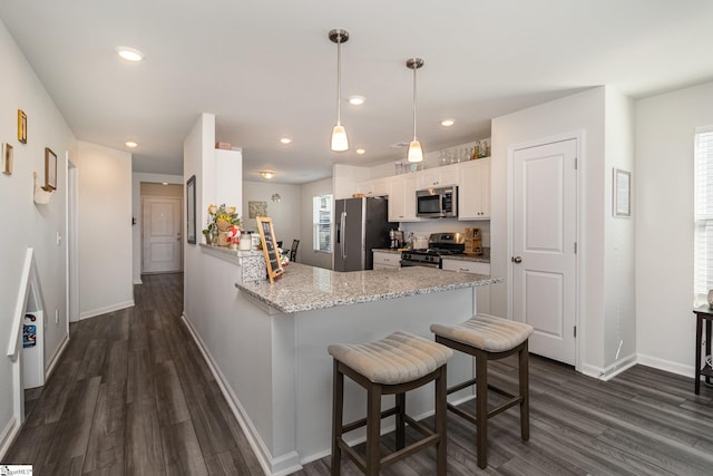 kitchen with appliances with stainless steel finishes, a kitchen breakfast bar, decorative light fixtures, white cabinetry, and kitchen peninsula