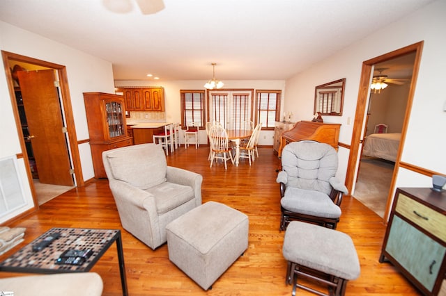 living room featuring ceiling fan with notable chandelier and light wood-type flooring