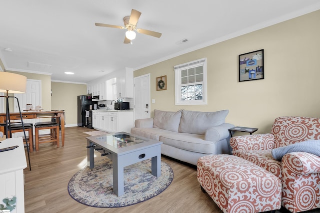 living room with sink, ornamental molding, ceiling fan, and light hardwood / wood-style flooring