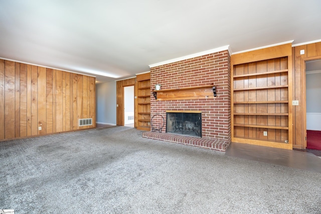 unfurnished living room with a brick fireplace, built in shelves, carpet floors, wood walls, and crown molding