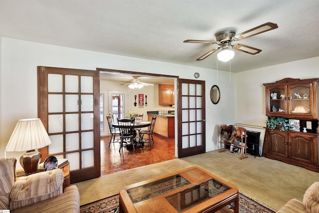 carpeted living room with french doors, ceiling fan, and a textured ceiling