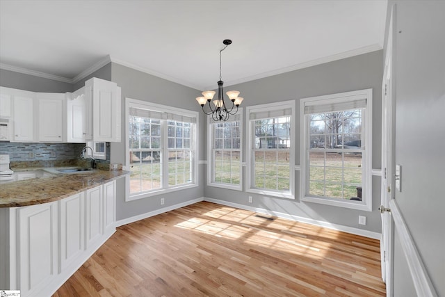 unfurnished dining area with light wood-type flooring, sink, a notable chandelier, and ornamental molding