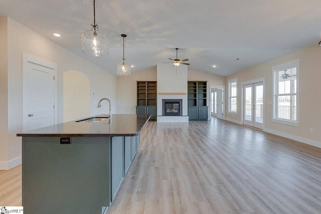 kitchen featuring vaulted ceiling, sink, light wood-type flooring, pendant lighting, and an island with sink