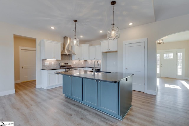 kitchen featuring white cabinetry, a center island with sink, wall chimney exhaust hood, and stainless steel stove