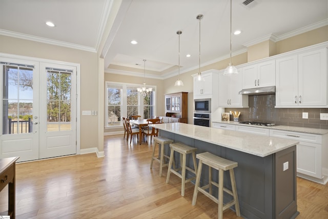 kitchen with white cabinetry, a kitchen island, light stone countertops, appliances with stainless steel finishes, and pendant lighting