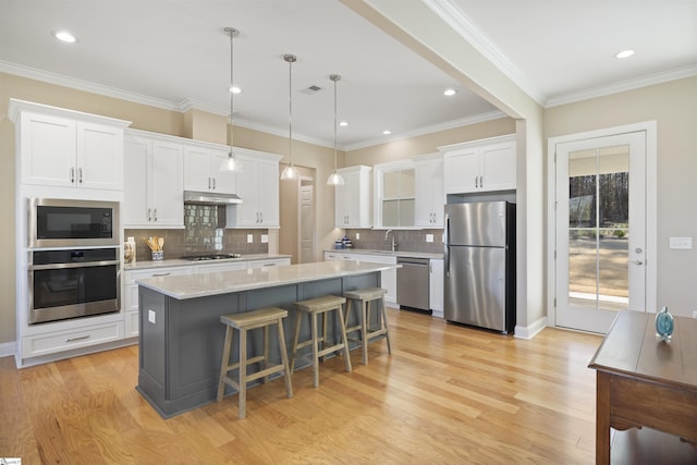 kitchen with white cabinetry, hanging light fixtures, a kitchen island, appliances with stainless steel finishes, and a kitchen bar