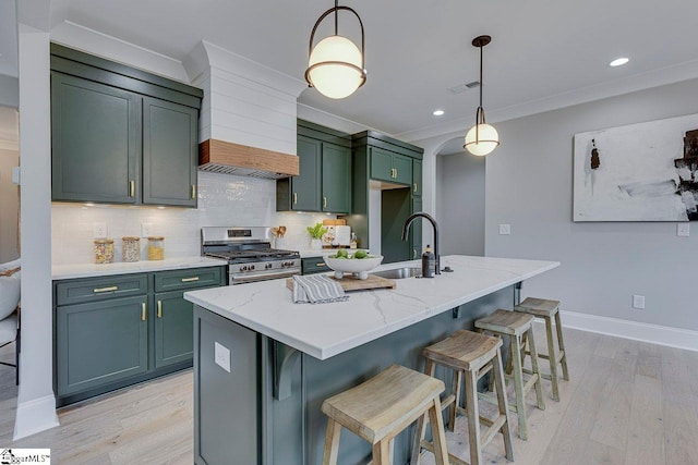 kitchen featuring light stone counters, premium range hood, pendant lighting, stainless steel gas stove, and an island with sink