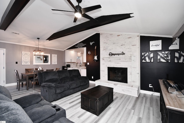 living room with a brick fireplace, light hardwood / wood-style flooring, lofted ceiling with beams, ceiling fan with notable chandelier, and crown molding