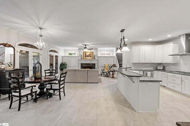 kitchen with appliances with stainless steel finishes, wall chimney exhaust hood, white cabinets, decorative light fixtures, and a lit fireplace