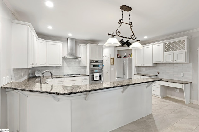 kitchen with wall chimney range hood, white cabinets, a breakfast bar, stainless steel appliances, and hanging light fixtures