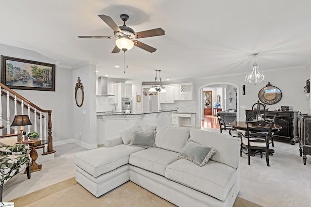 living room with stairway, arched walkways, ornamental molding, and ceiling fan with notable chandelier