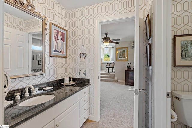 bathroom with ceiling fan, baseboards, vanity, toilet, and wallpapered walls