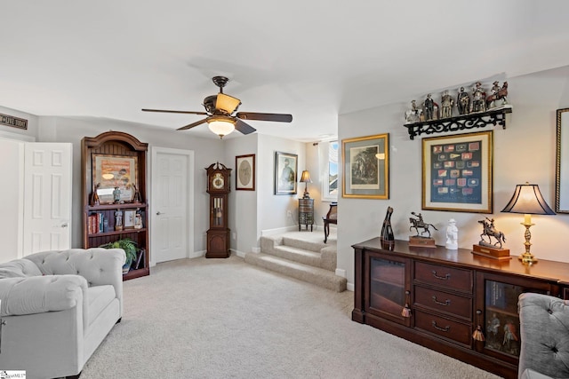 sitting room with stairway, light carpet, a ceiling fan, and baseboards