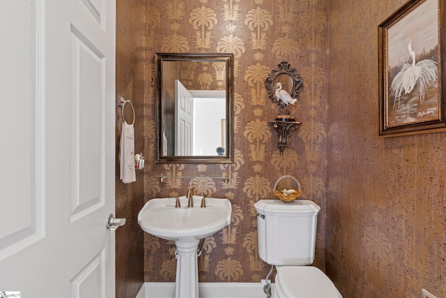 bathroom with wallpapered walls, toilet, and a sink