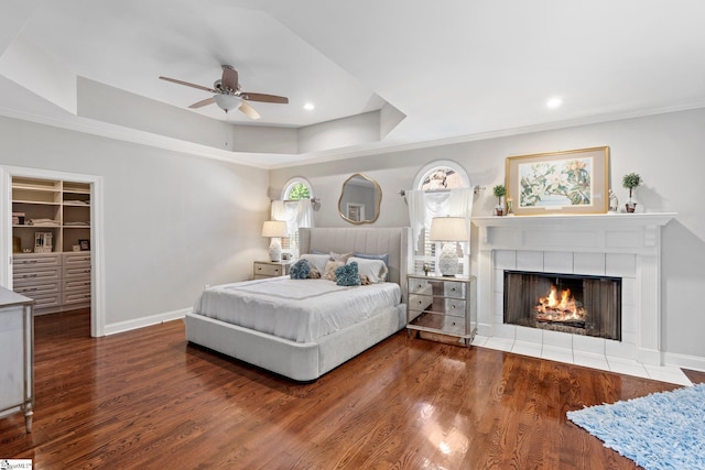 bedroom with baseboards, a tile fireplace, wood finished floors, and a tray ceiling