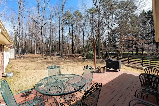 wooden terrace with a lawn, a trampoline, outdoor dining area, and fence