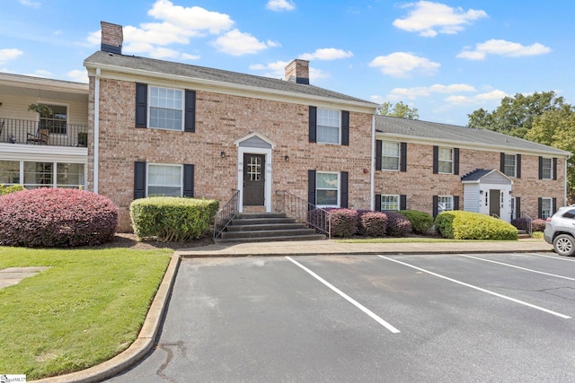 view of front of home featuring brick siding, a chimney, a front lawn, and uncovered parking