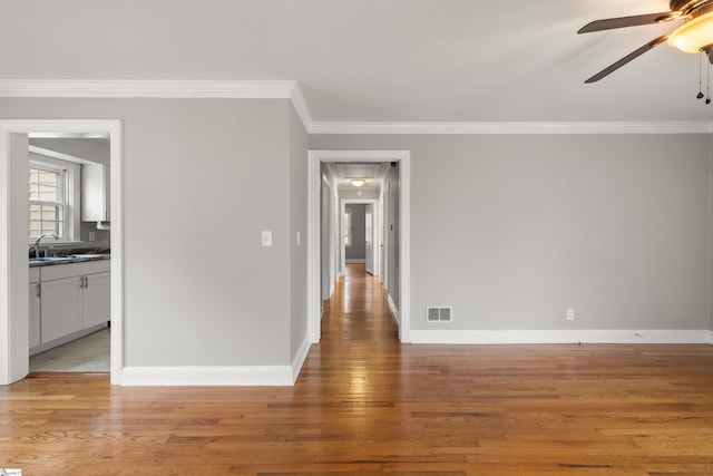 unfurnished room with attic access, baseboards, ornamental molding, a sink, and light wood finished floors