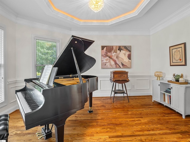 sitting room with a raised ceiling, a chandelier, light wood-style flooring, and a decorative wall