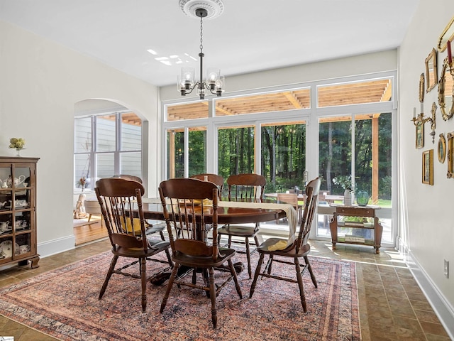 dining room with arched walkways, a chandelier, and baseboards