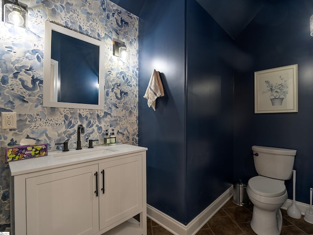 half bath featuring vanity, baseboards, tile patterned flooring, wallpapered walls, and toilet