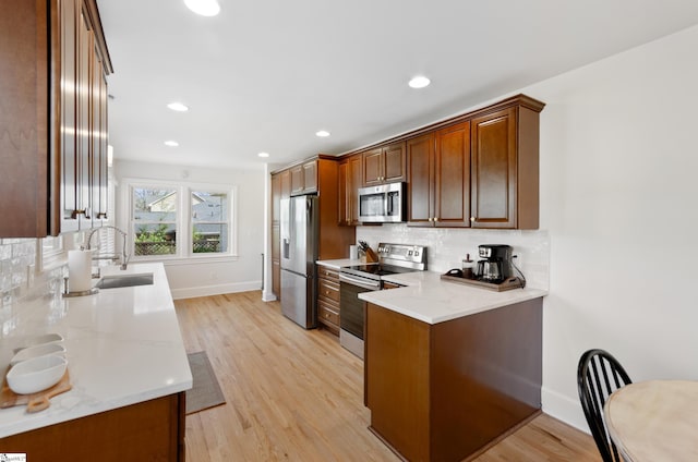 kitchen featuring stainless steel appliances, light wood-style floors, a sink, and light stone counters