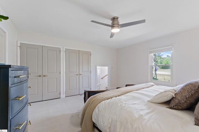 bedroom featuring light colored carpet, ceiling fan, and two closets