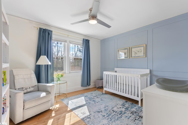 bedroom with a ceiling fan, a nursery area, a decorative wall, and light wood-style flooring