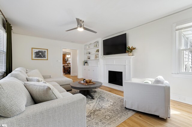 living area featuring built in features, a fireplace, ceiling fan, and wood finished floors