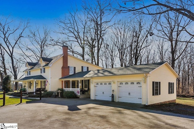 view of side of home with an attached garage, driveway, a chimney, and a porch