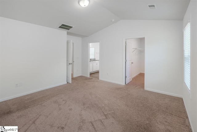 unfurnished bedroom featuring light colored carpet, lofted ceiling, a walk in closet, and visible vents