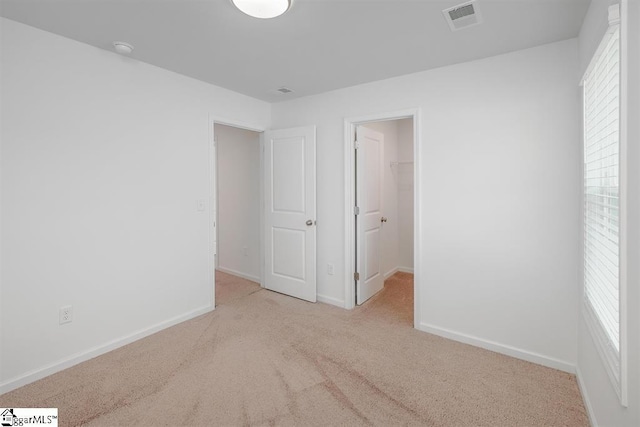 unfurnished bedroom with light colored carpet, visible vents, a spacious closet, and baseboards